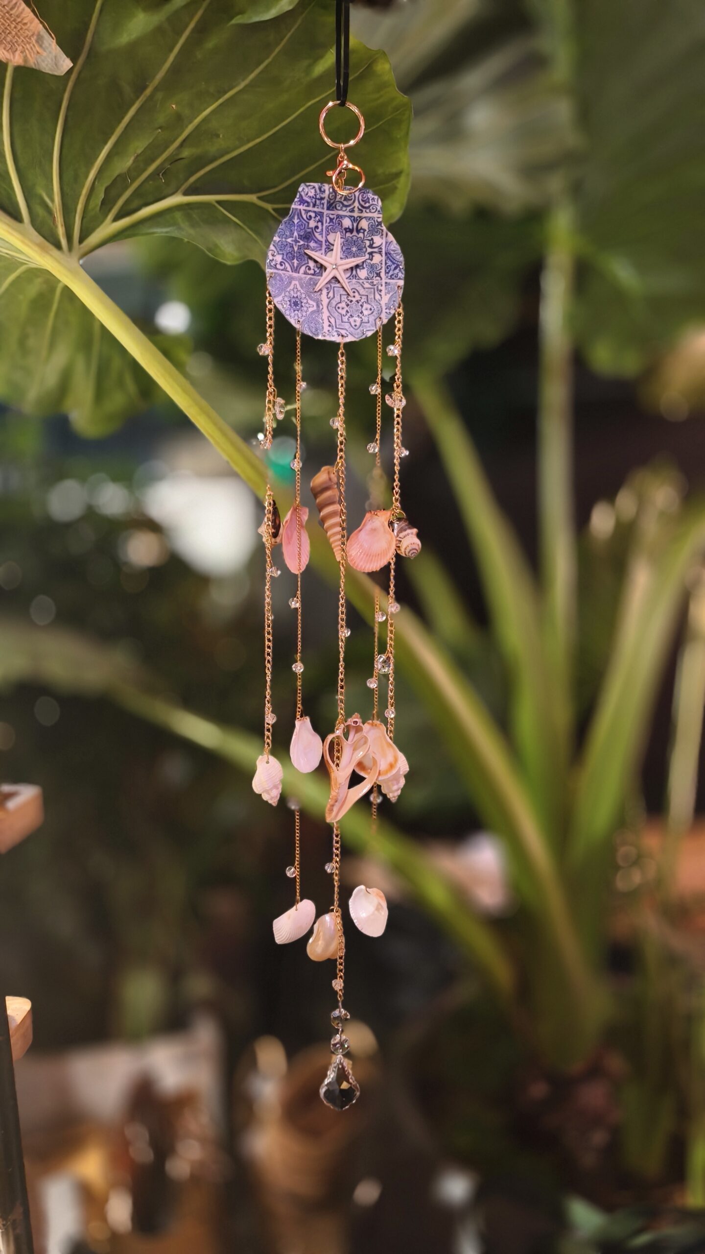Handmade Azulejos coastal shell suncatcher by Panda Crafts with blue-and-white ornamental design, starfish detail, real seashells and metallic chains.